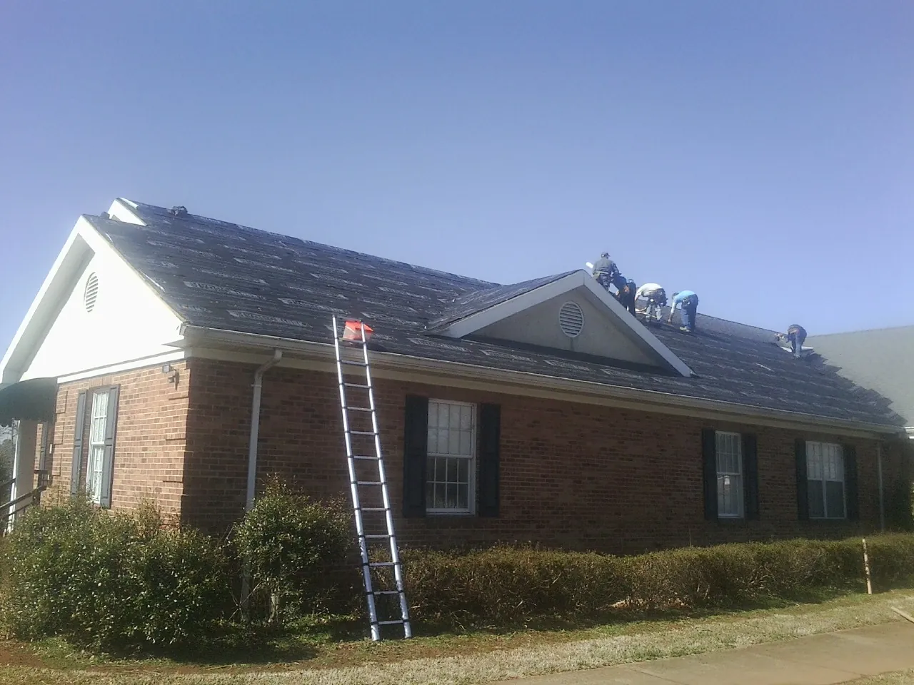 Crew tearing shingles off a brick ranch roof with a ladder set — Metal Roof Repair work by our crew in King William