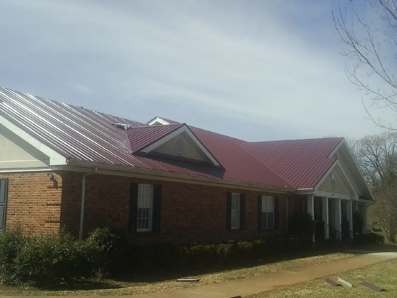 Red metal roof with gabled entries on a long brick building, from a Hail Damage Roof Repair job in King William