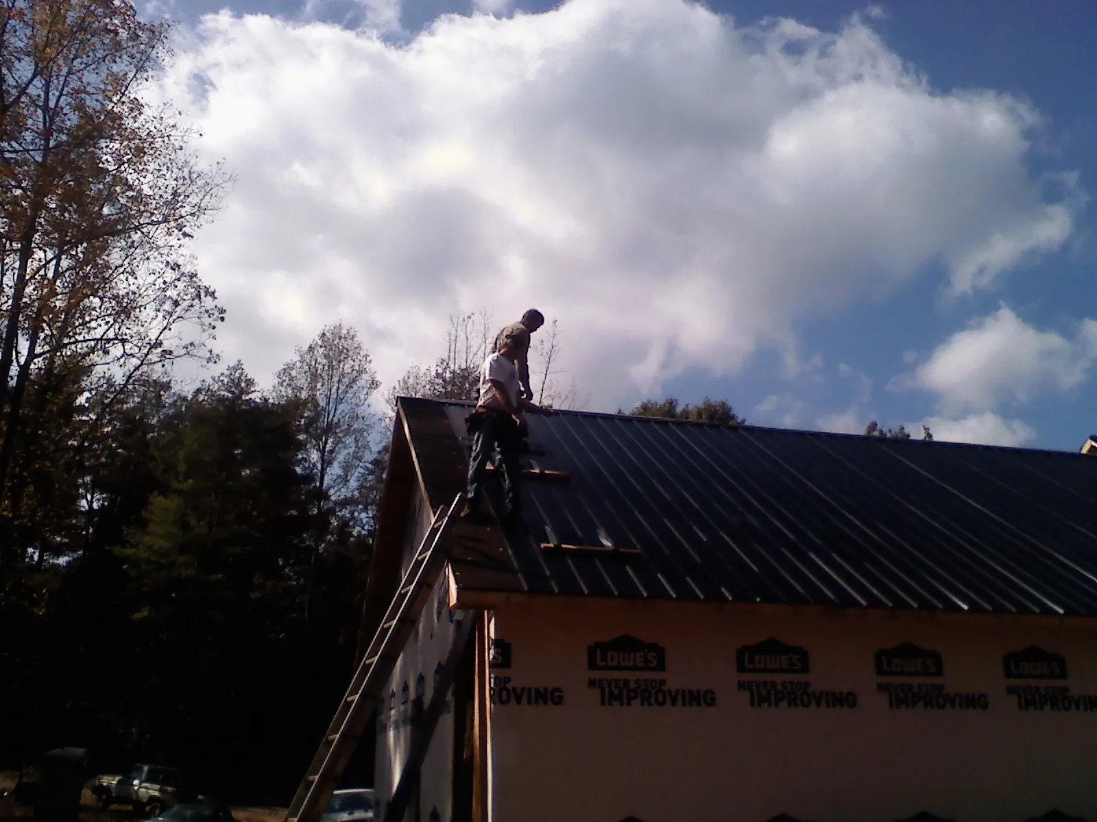 Roofer fastening dark metal panels high against a cloudy sky, from a Roof Inspection job in King William
